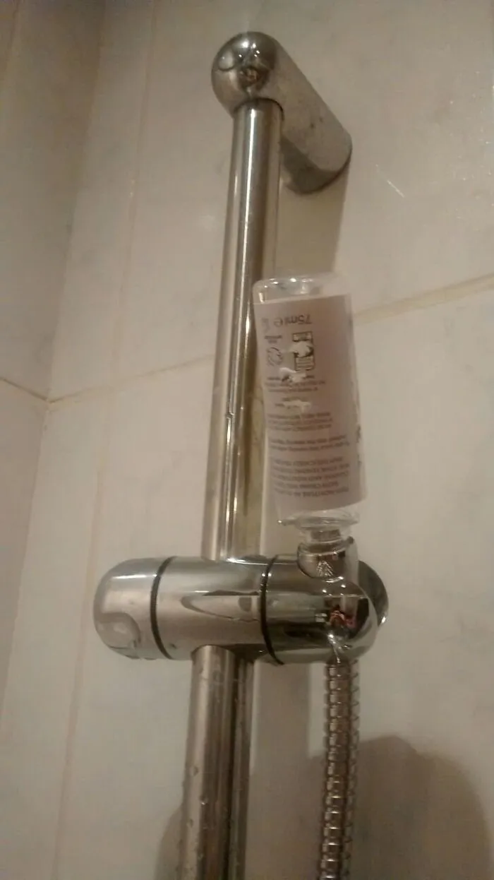 A shower head holder with a plastic bottle used as a makeshift repair, demonstrating a home renovate fail