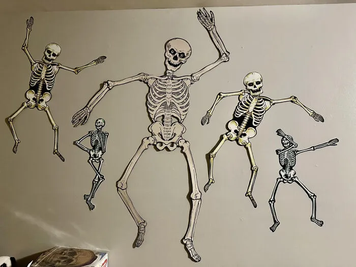 Paper skeletons in funny poses on a wall for Halloween decor.