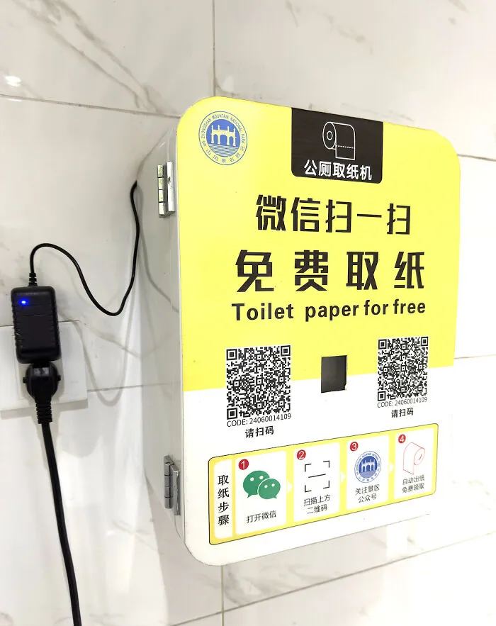 Absurd public toilet paper dispenser that requires scanning a QR code to unlock paper.