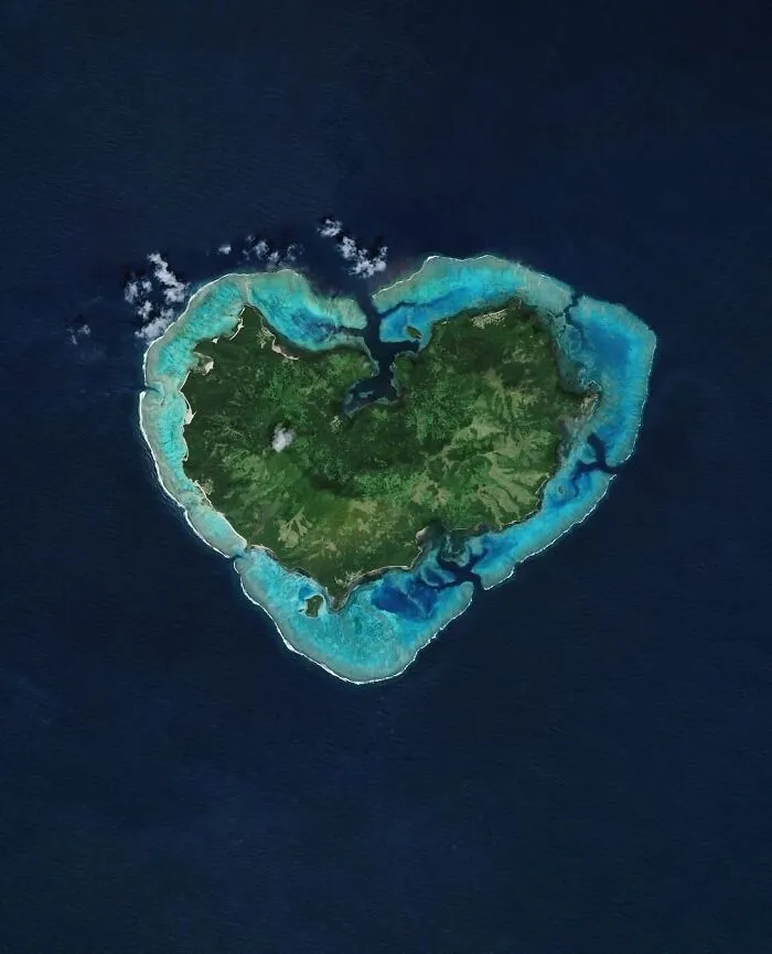 Surreal satellite photo of a heart-shaped tropical island in the ocean.