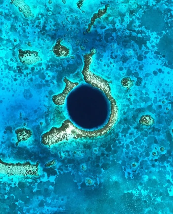 Aerial view featuring a deep blue ocean sinkhole surrounded by turquoise waters, captured in a satellite photo.