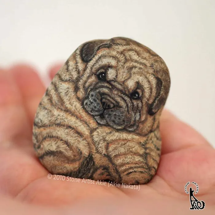 Stone painting of a realistic wrinkly pug dog resting in an open palm