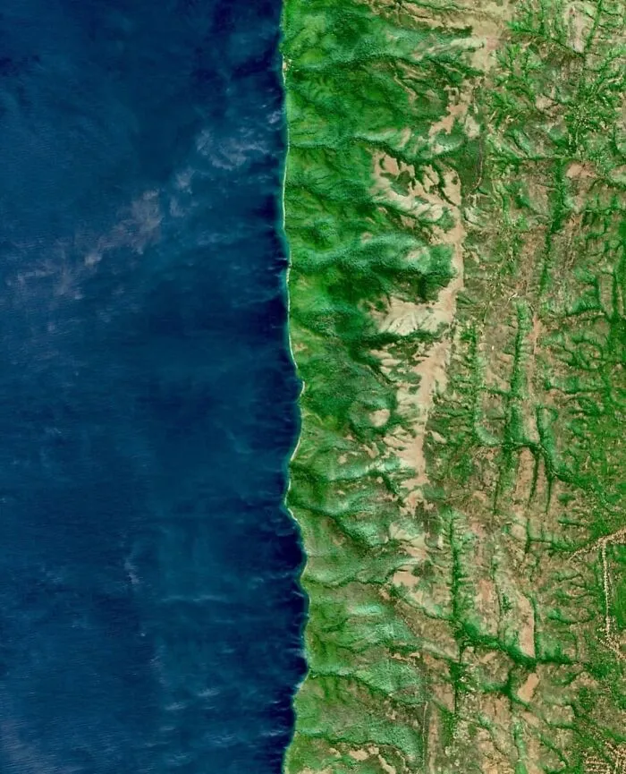 A high-angle satellite photo displaying a vibrant green coastline bordered by deep blue ocean waters.