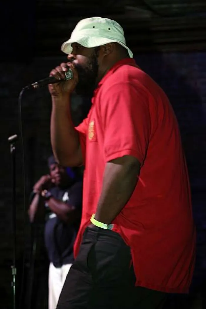 A man in a red shirt and bucket hat performing on stage with a microphone captured in photo for the last time