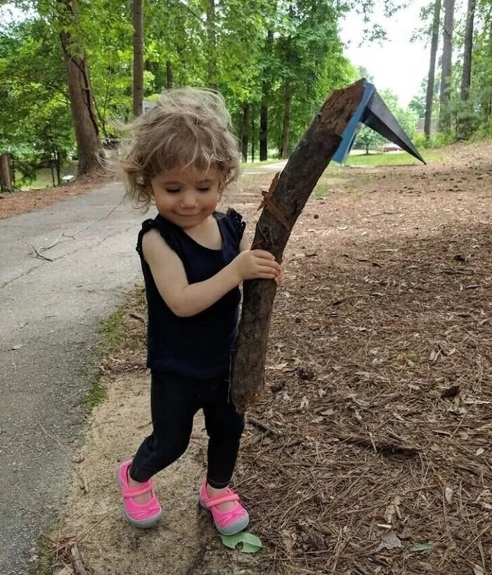 Perspective photo of a toddler holding a wooden stick that looks like a grim reaper scythe.