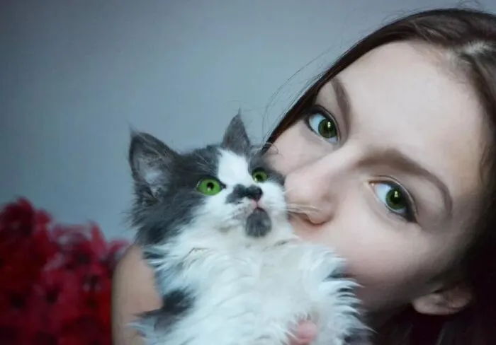 Optical illusion photo of a girl with green eyes holding a matching fluffy kitten next to her face