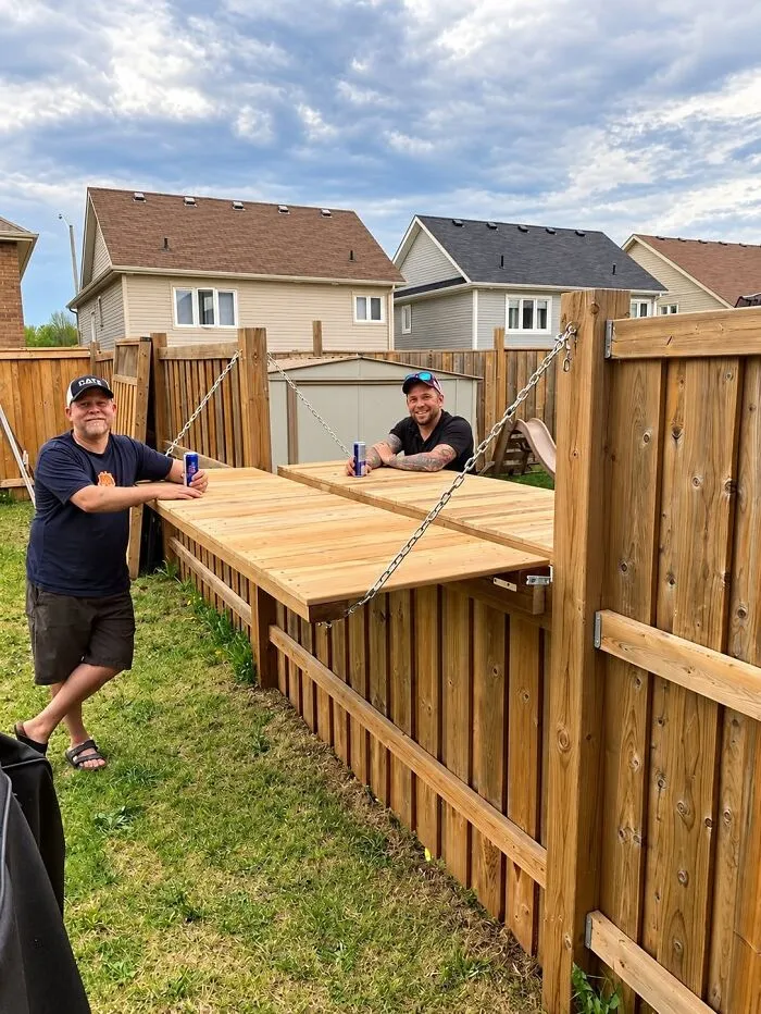 Two men leaning on a wooden fence table, showcasing clever wooden creations.