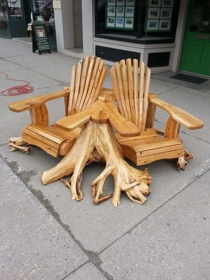 Two outdoor wooden chairs connected by a natural tree root table representing clever wooden creations.