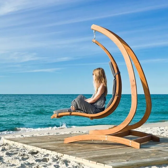 Woman relaxing on a crescent-shaped wooden hanging lounge chair on the beach.