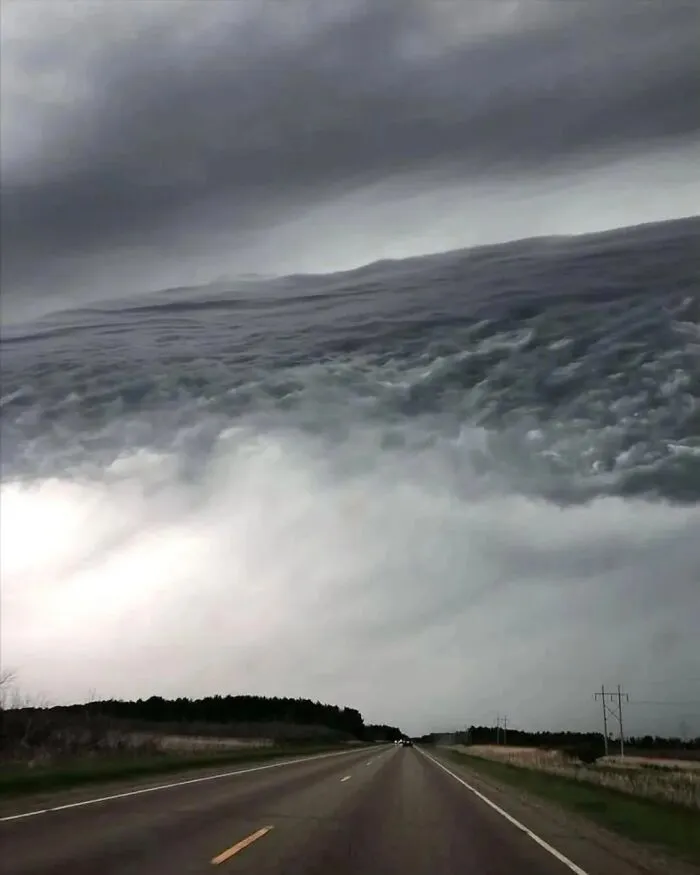 Dark cloud formations over a highway create a ocean wave illusion, a photo that plays tricks on your eyes.
