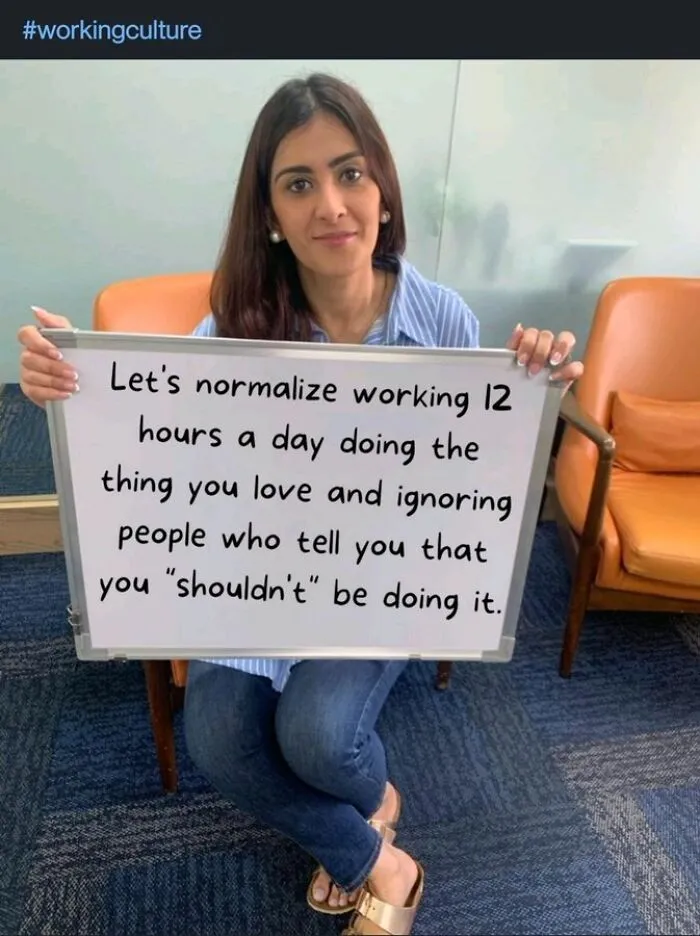 Woman holding sign about normalizing working 12 hours a day in working culture