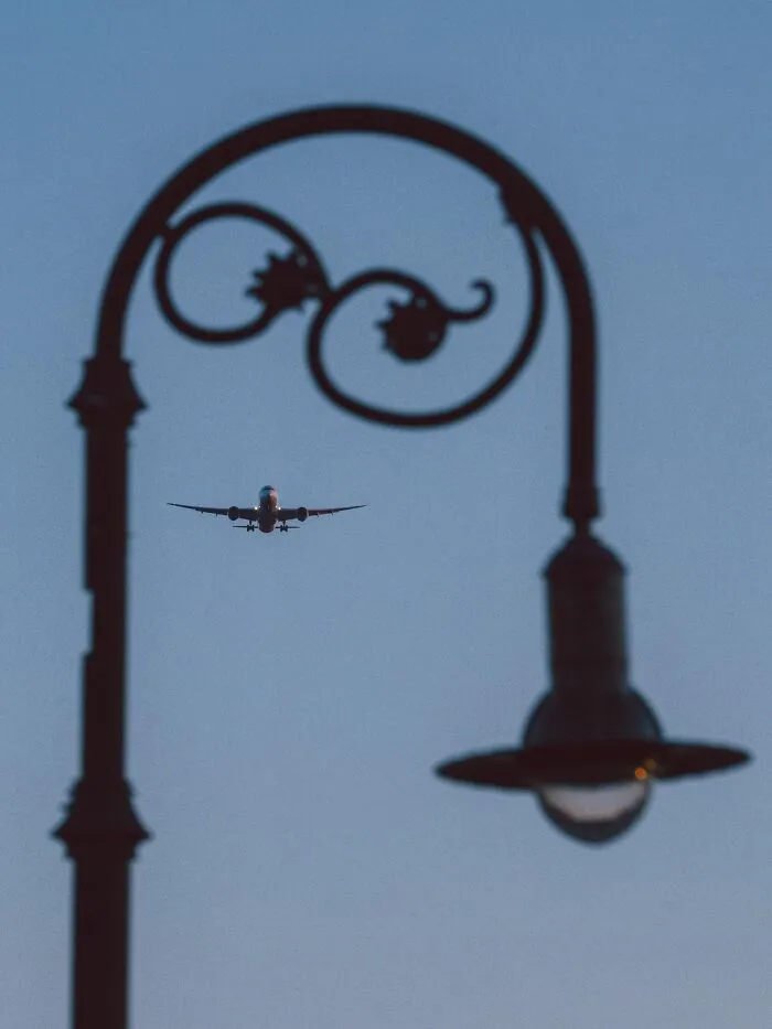 A photo of a distant airplane aligned perfectly with a street lamp curve