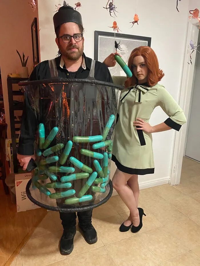 A man in a jar of pills costume stands next to a woman in a green dress for Halloween couples costumes