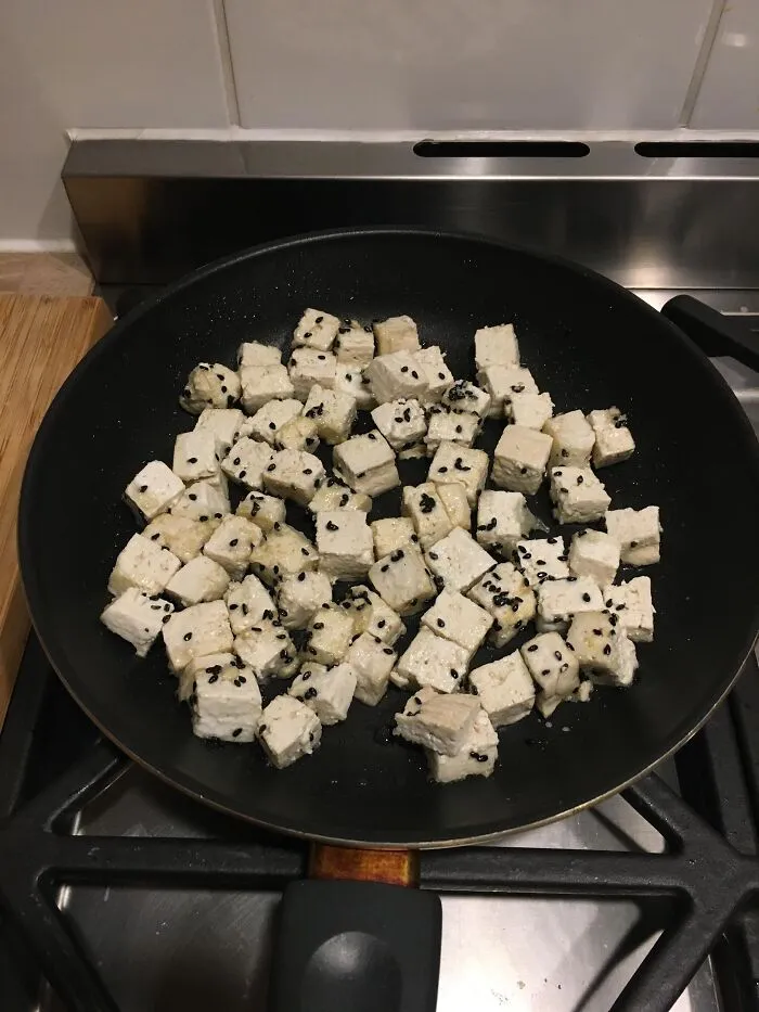 Cubic tofu sprinkled with black sesame seeds in a pan, confusing eyes playing tricks with dice lookalikes.