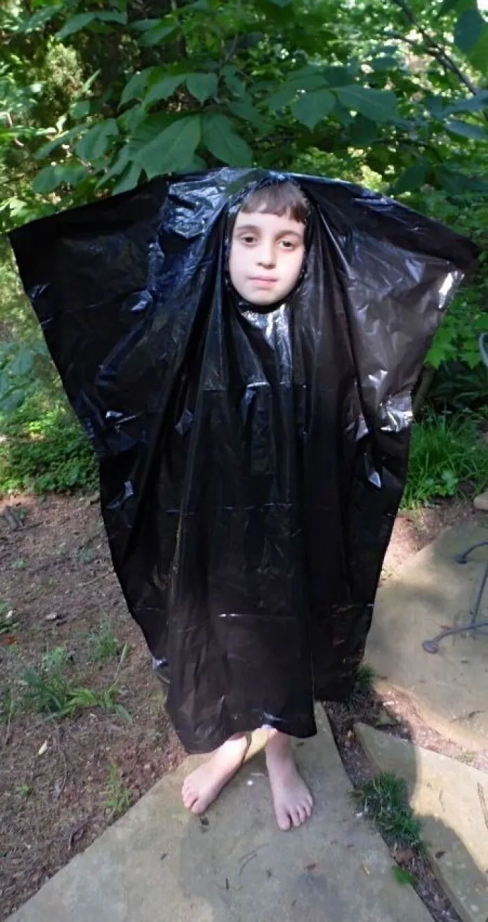 Funny Halloween photo of a kid wearing a black trash bag as a budget costume outdoors.