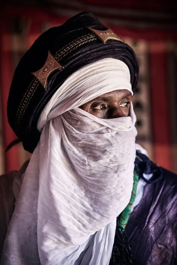 A portrait photo of a Tuareg man in a traditional white turban and veil looking aside