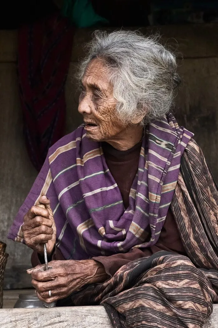 A portrait photo showing the deep expression of an elderly woman holding a tool while looking away