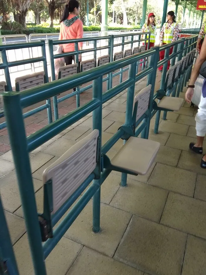 Ingenious things: Foldable seats attached to a green queue barrier at a public waiting area.