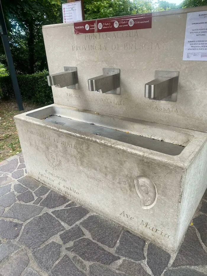 Public stone drinking fountain with three metal taps in Brescia, Italy, showcasing useful and ingenious things.