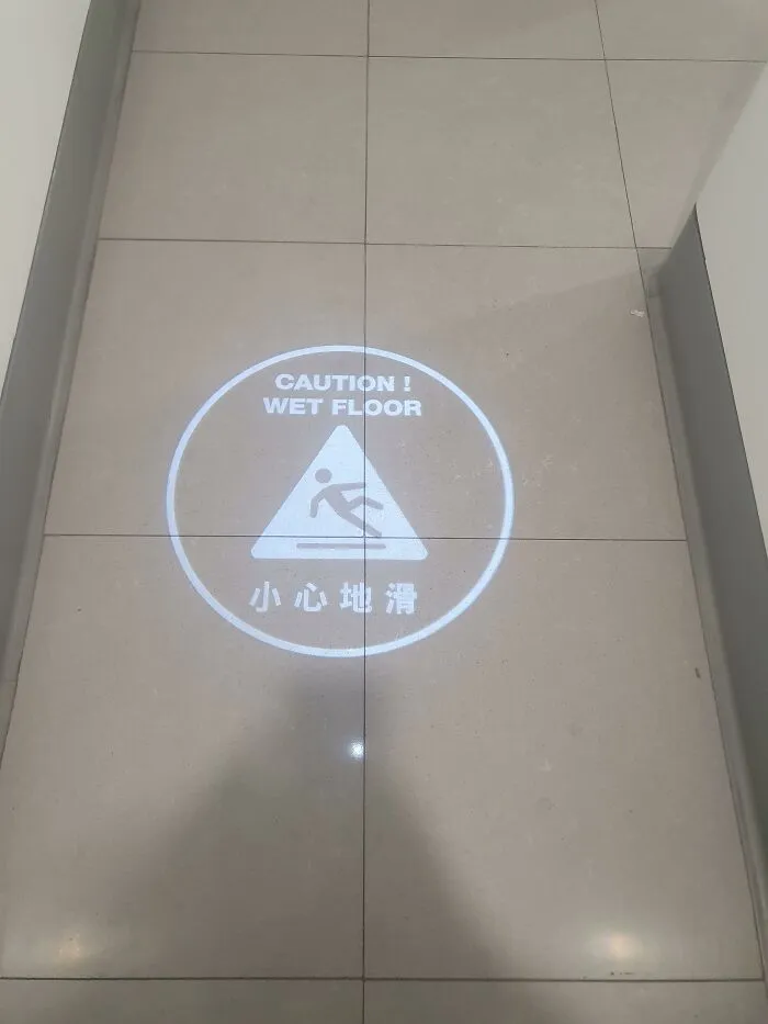 A projected wet floor warning sign on tiled flooring, showcasing ingenious things in various parts of the world.
