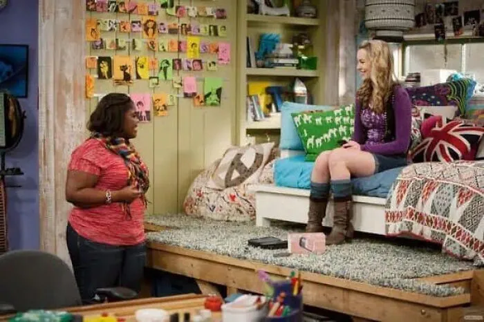 Two girls talking on a television set surrounded by colorful movie props