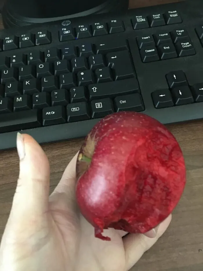 A creepy photo of a hand holding a red apple with an unusually deep, raw-looking bite mark.