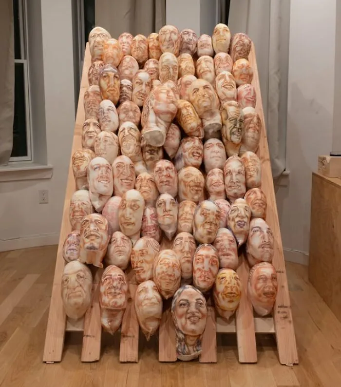 An installation of uncanny ceramic faces arranged on a wooden frame, giving a creepy photo vibe.