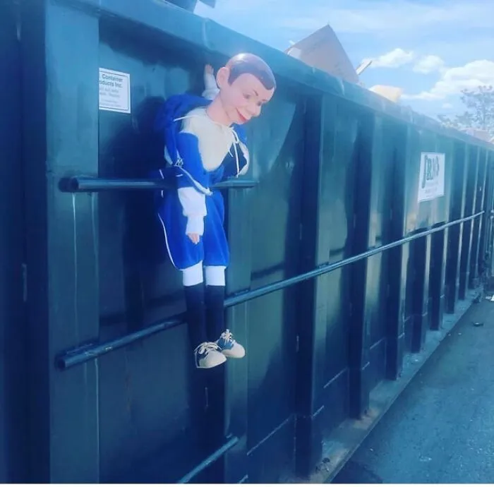A dummy doll hanging on a metal dumpster among creepy photos