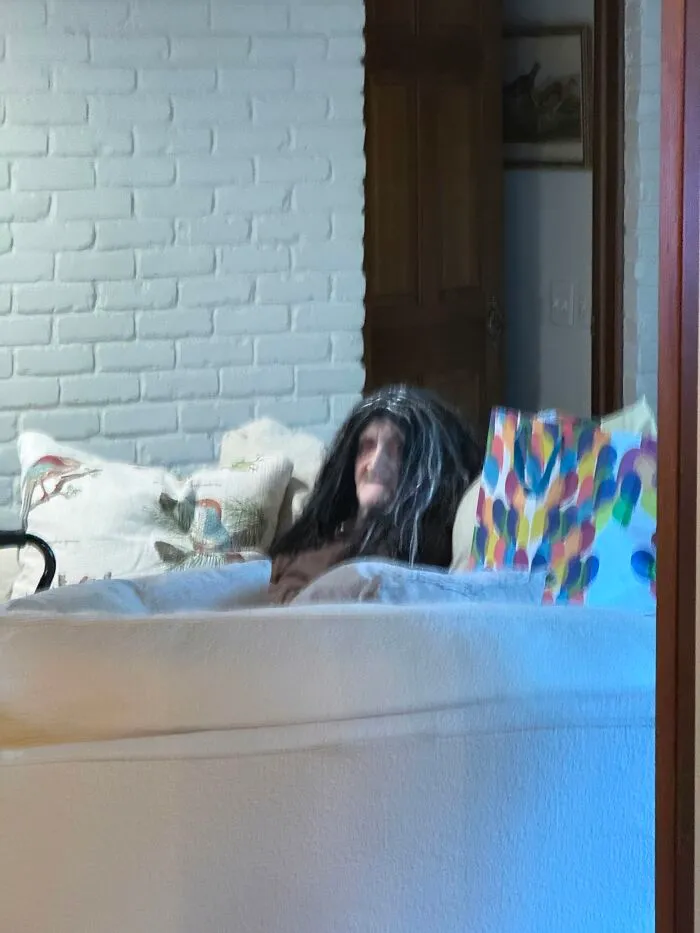 An eerie figure wearing a long black wig sitting on a couch, creating creepy photos.