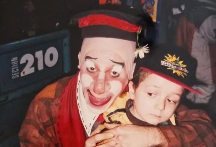 A creepy photo of a man dressed as a clown hugging a young boy who looks uncomfortable.