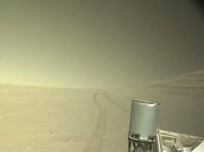 A slightly creepy photo of tracks leading across a desolate, hazy landscape on Mars