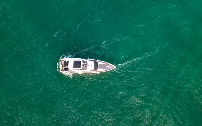 Aerial top down view of a yacht cruising on green water for worst case scenarios stories.