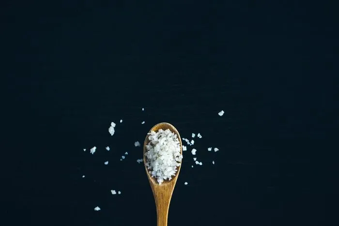 A wooden spoon filled with coarse sea salt on a dark background, sharing brilliant tips for seasoning.