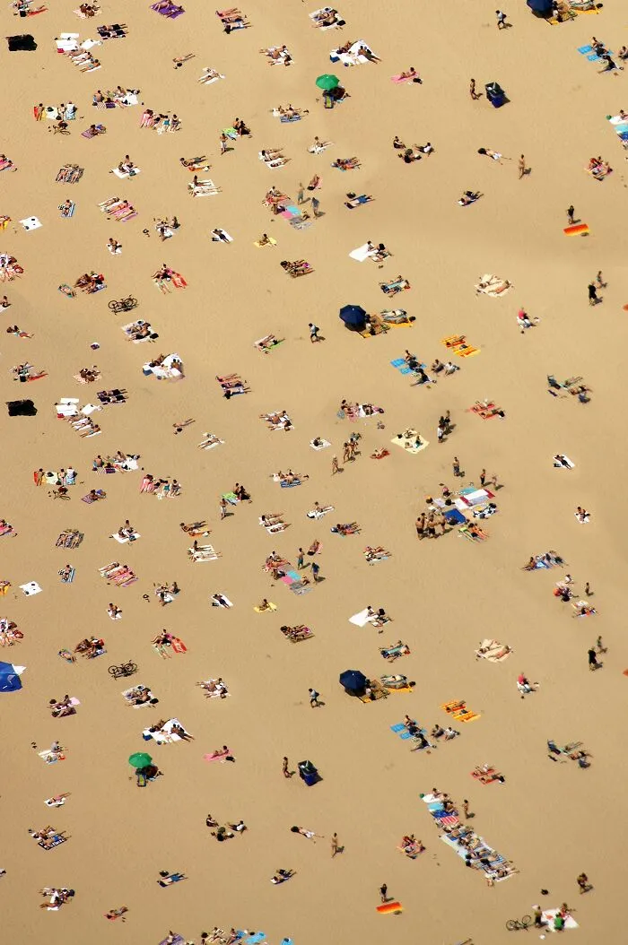 An aerial view of a crowded sandy beach with people sharing space under umbrellas.