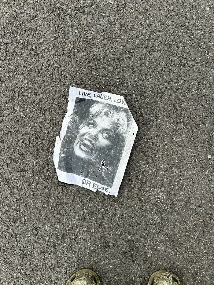 A crumpled paper flyer on asphalt reading Live, Laugh, Love OR ELSE, an example of lost and forgotten messages.