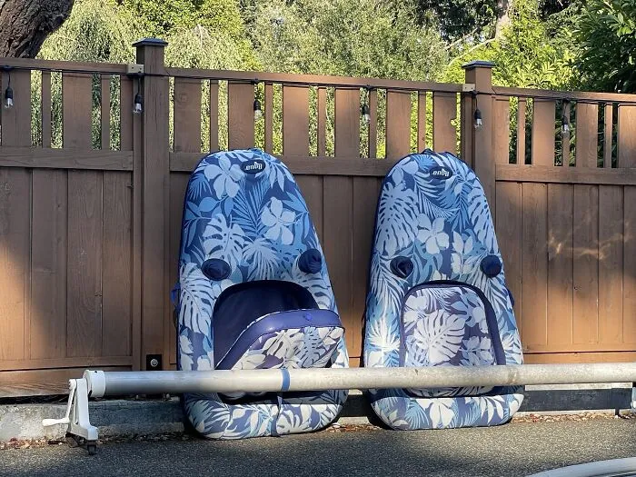 Two inflatable blue pool loungers leaning against a wooden fence, one absurd moment showing a seat upside down.