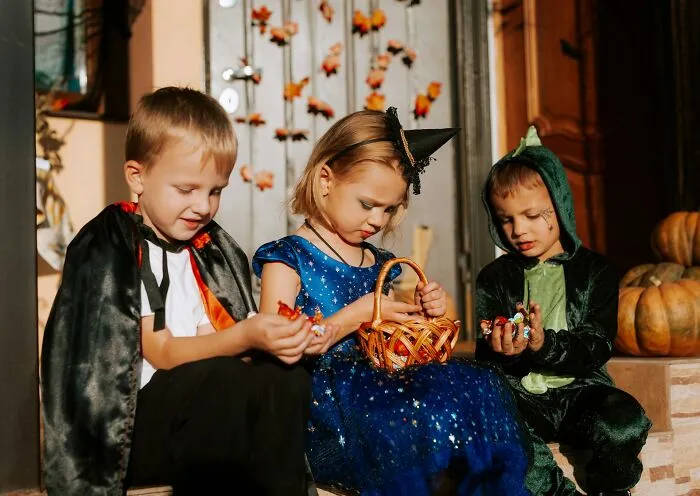 Children dressed in Halloween costumes sitting together and looking at their trick-or-treat candy.