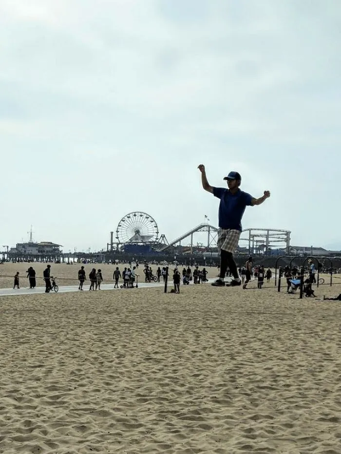 A man slacklining on a sandy beach creating perfectly confusing optical illusions with the pier background.