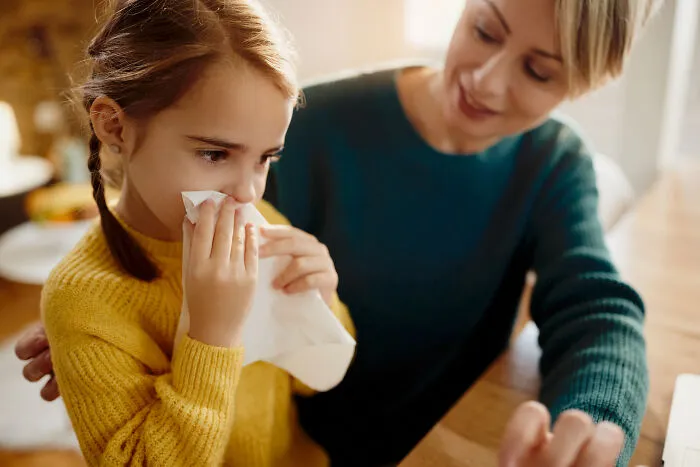 An overprotective mother helping her daughter blow her nose, highlighting helicopter parenting traits.