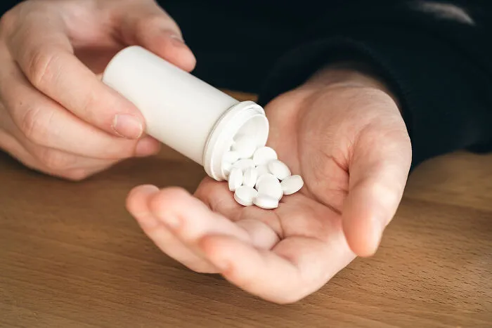 Close-up of a person pouring white pills into their hand, reflecting experiences of people feeling sick.