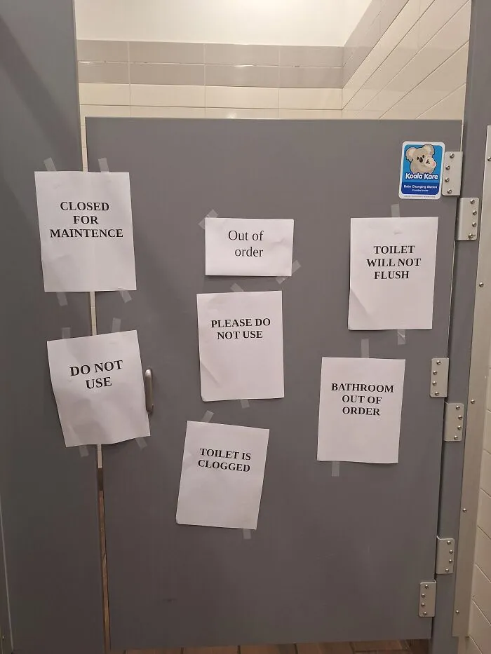 Absurd signs plastered on a bathroom stall door repeating that it is out of order