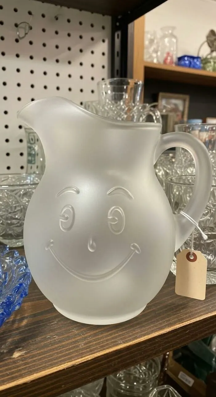 Frosted glass Kool-Aid pitcher sitting on a wooden shelf, a iconic piece of '80s kids nostalgia.