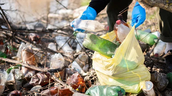 Volunteer wearing blue gloves collecting plastic waste in a bag, highlighting environmental PR stunts.