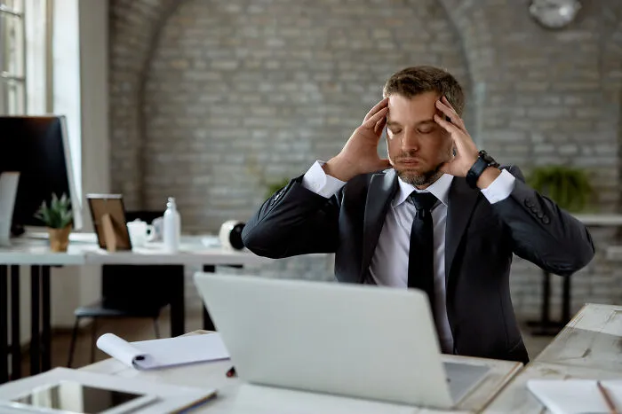 Stressed businessman sitting at a computer desk holding his head