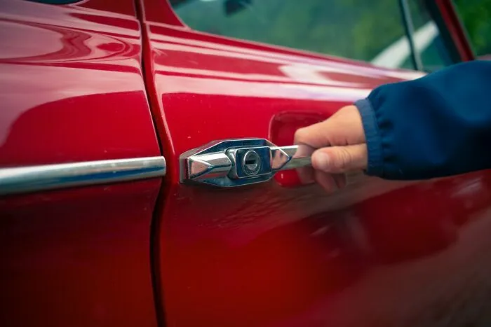 A person reaching to open a red vintage car door, representing escaping relationship fights.