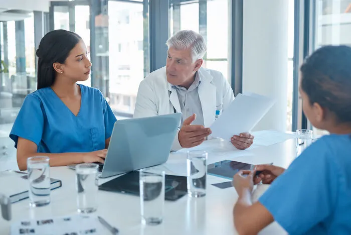 Medical staff in blue scrubs discussing paperwork around a table representing people's jobs