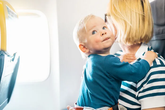A toddler held by his mother next to the window of seats on flights