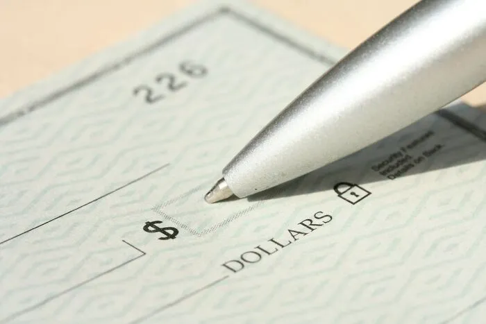 Close-up of a pen writing on a dollar check, symbolizing petty relationship fights over money.