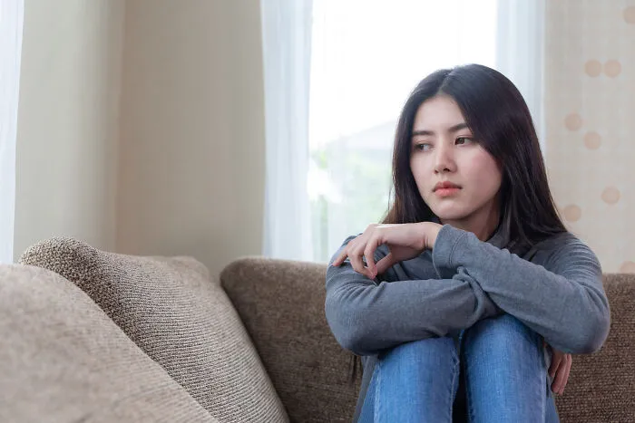 A sad young woman sitting on a couch, reflecting on words from narcissistic parents.