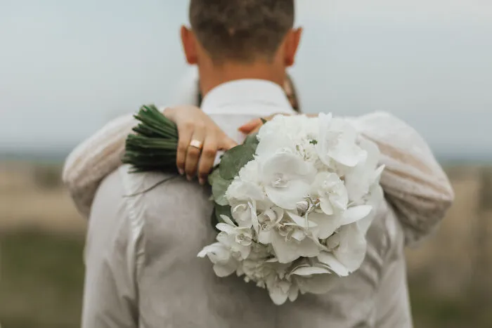 A bride holding a white flower bouquet while hugging the groom, taken from a wedding before a divorce.